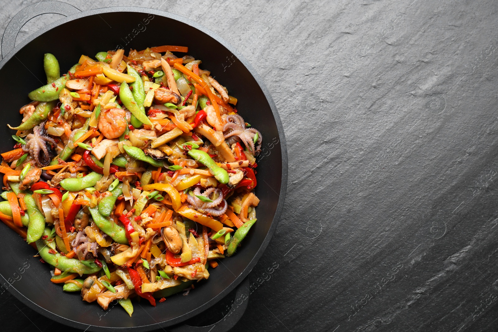 Photo of Stir-fry sea food in wok on grey textured table, top view. Space for text