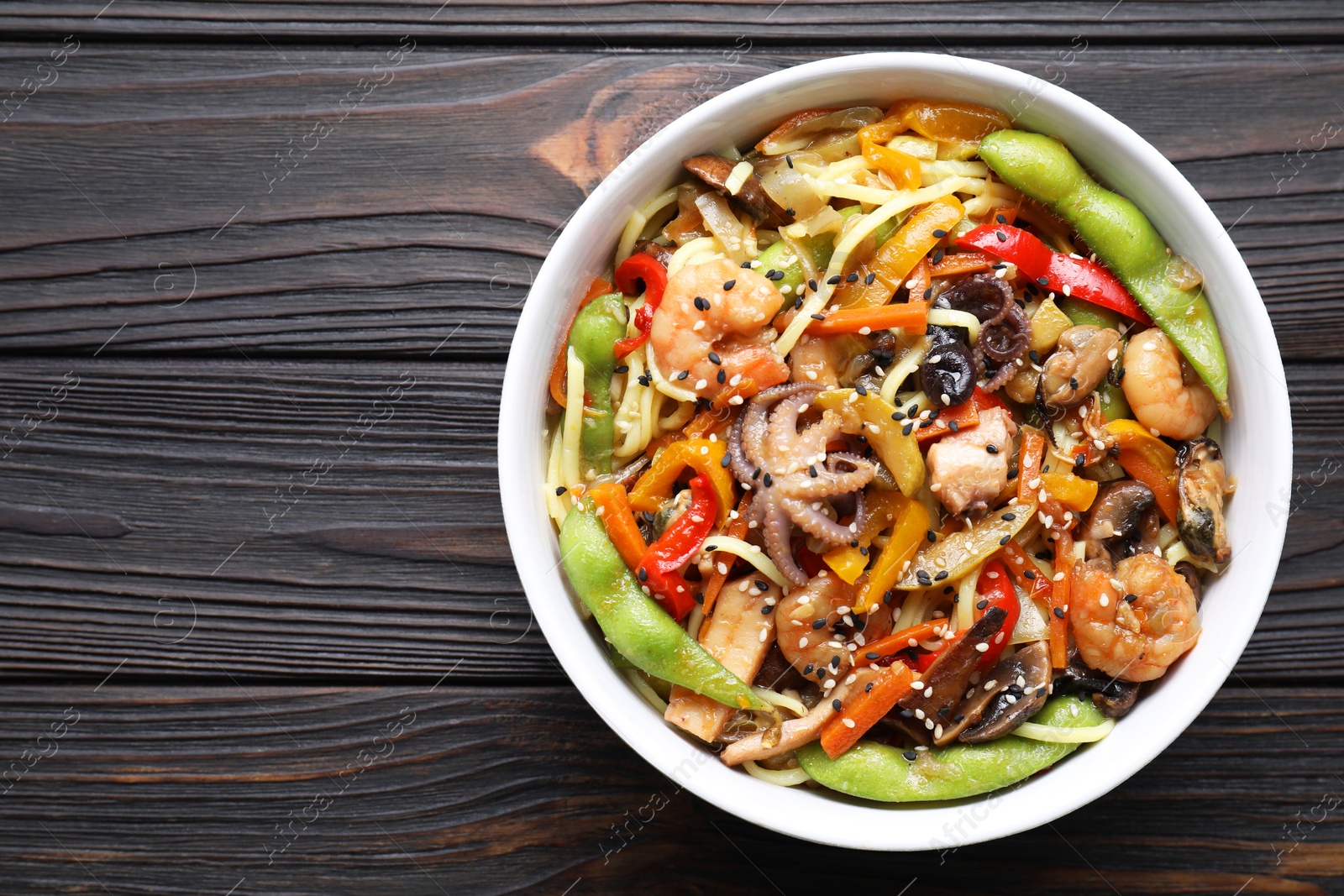 Photo of Stir-fry noodles with sea food in bowl on wooden table, top view. Space for text