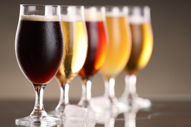 Photo of Glasses with different types of beer and ice cubes on mirror surface, closeup