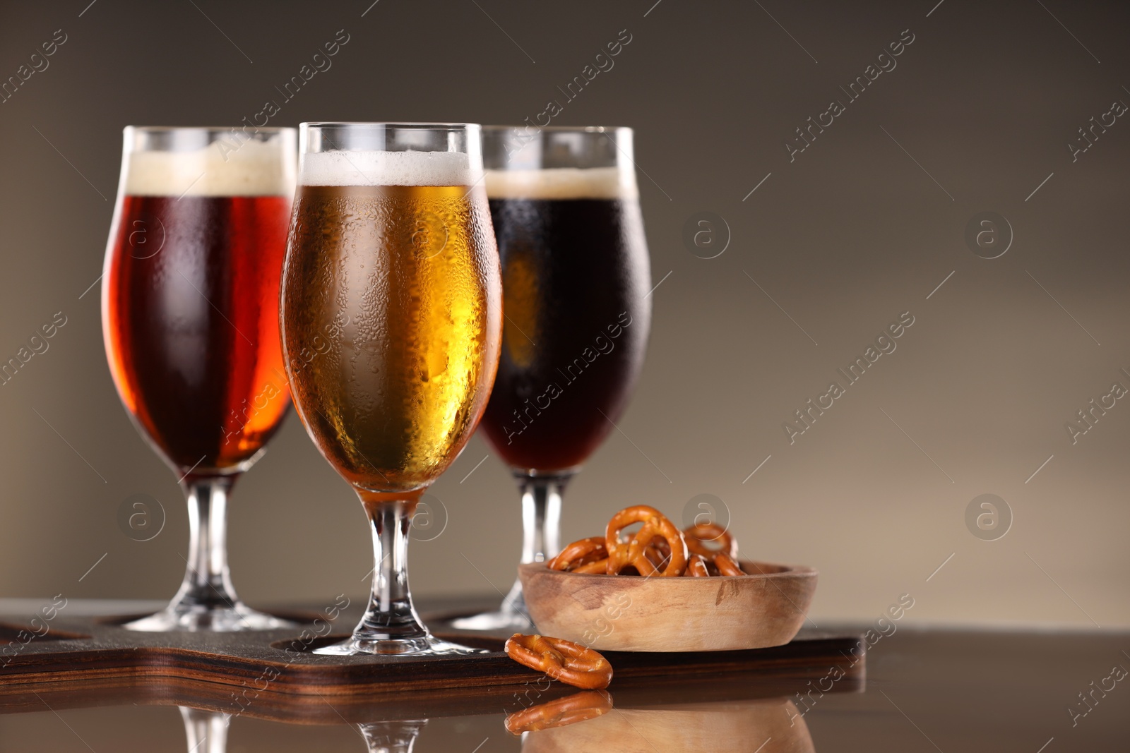 Photo of Glasses with different types of beer and snacks on mirror surface, closeup. Space for text