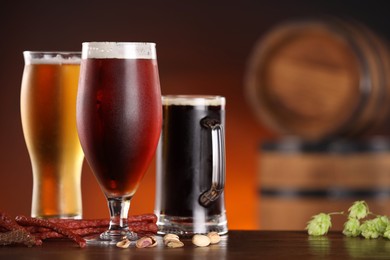 Photo of Glasses with different types of beer, snacks and fresh hops on wooden table in bar. Space for text