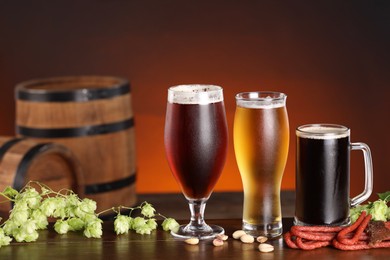 Photo of Glasses with different types of beer, snacks and fresh hops on wooden table in bar