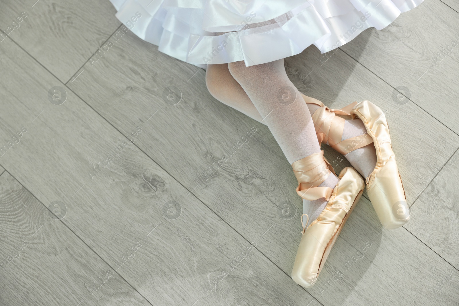 Photo of Little ballerina wearing pointe shoes on floor indoors, top view. Space for text