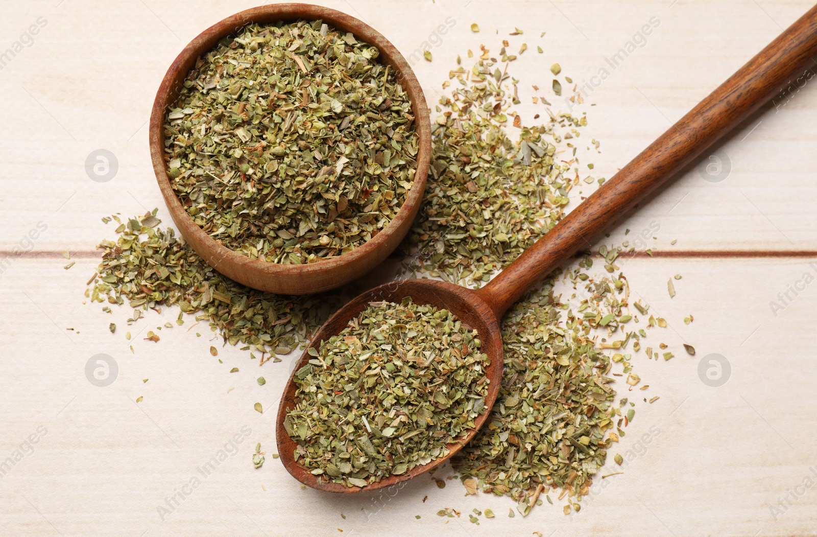 Photo of Dried oregano in bowl and spoon on wooden table, top view