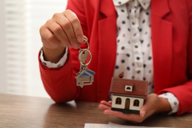 Photo of Real estate agent with house model and key at wooden table, closeup