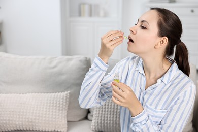 Photo of Young woman taking CBD tincture indoors, space for text