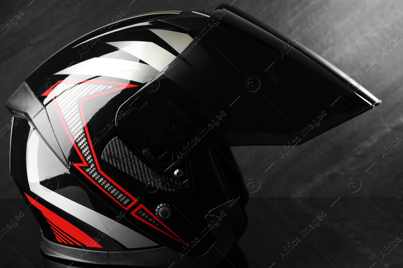 Photo of Modern motorcycle helmet with visor on dark gray background, closeup