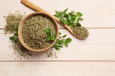 Photo of Dried oregano in bowl, spoon and green leaves on wooden table, top view