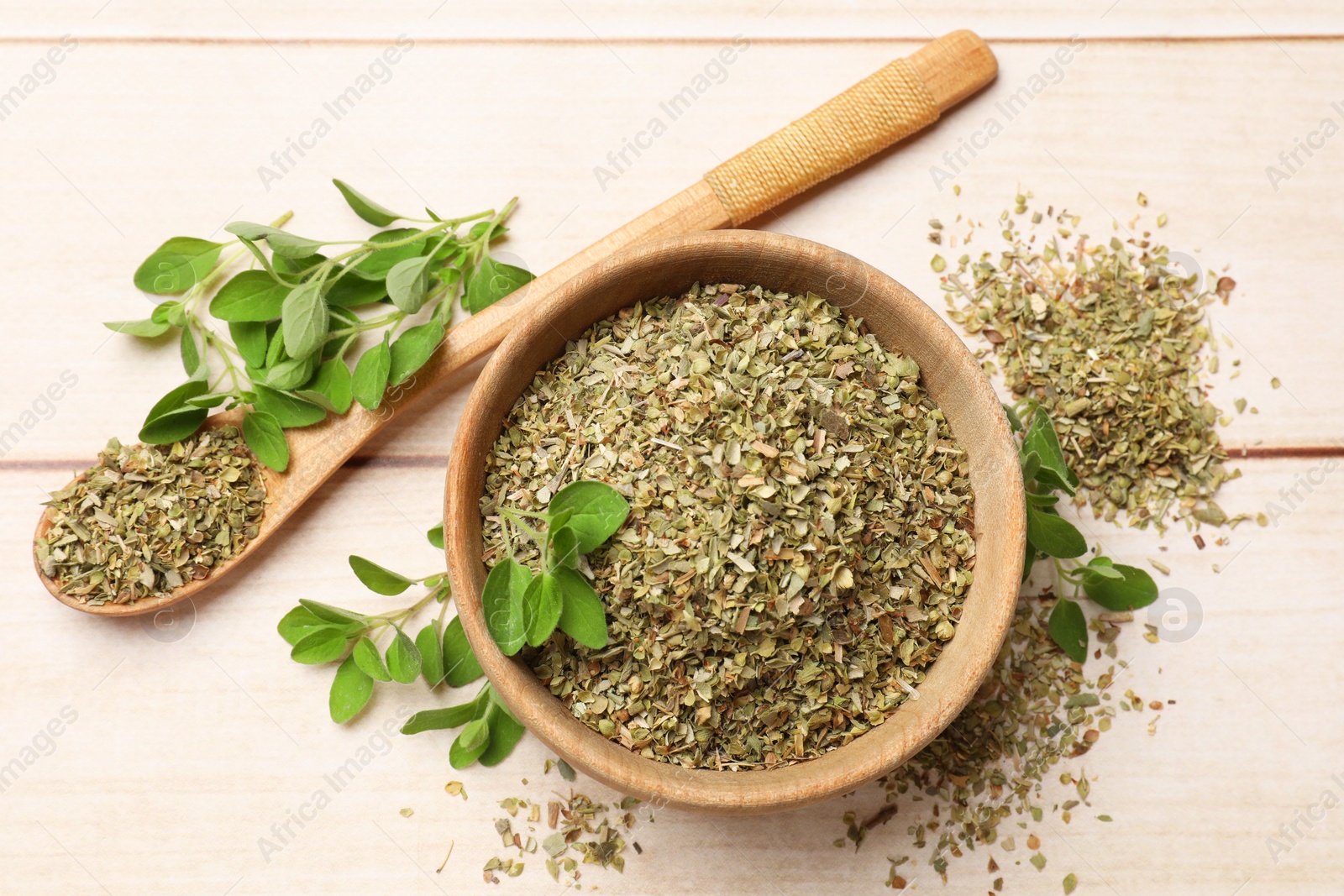 Photo of Dried oregano in bowl, spoon and green leaves on wooden table, top view