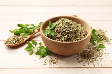 Photo of Dried oregano in bowl, spoon and green leaves on wooden table