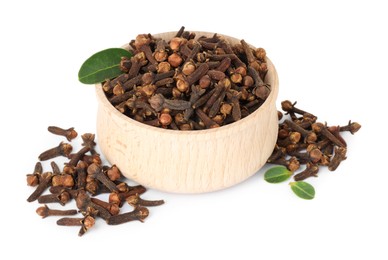 Photo of Dry clove buds in wooden bowl and green leaves on white background. Aromatic spice