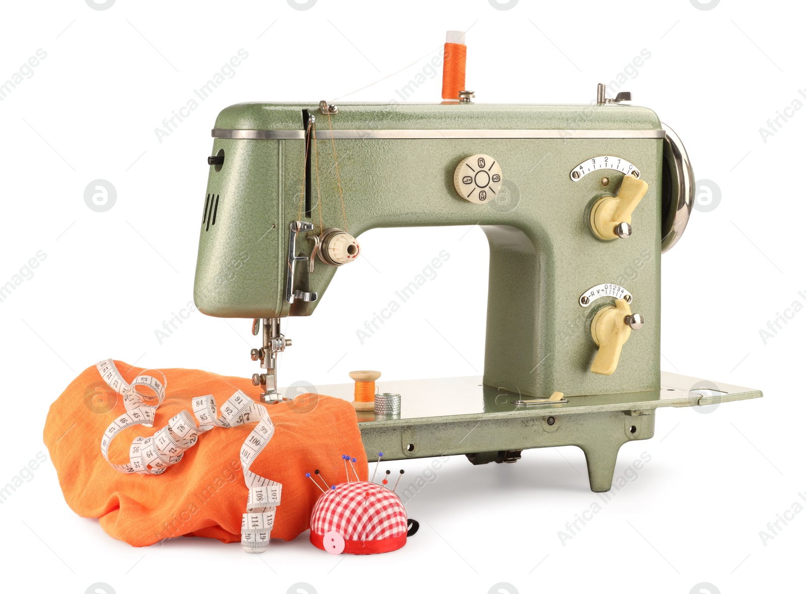 Photo of Sewing machine with orange fabric, measuring tape, pincushion and spools of threads isolated on white