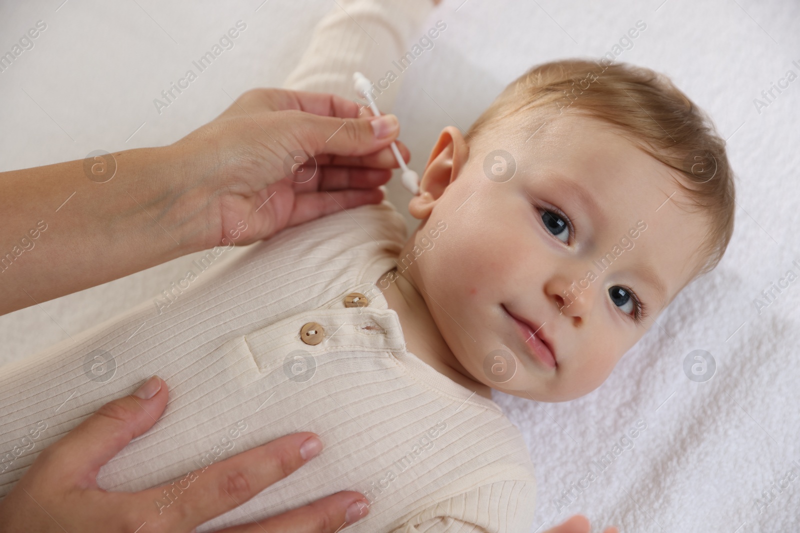 Photo of Mother cleaning ear of her cute little baby with cotton swab on bed, closeup