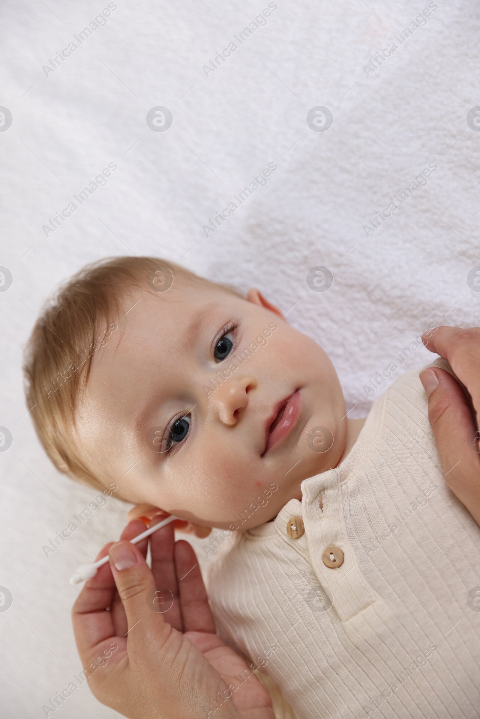 Photo of Mother cleaning ear of her cute little baby with cotton swab on bed, top view