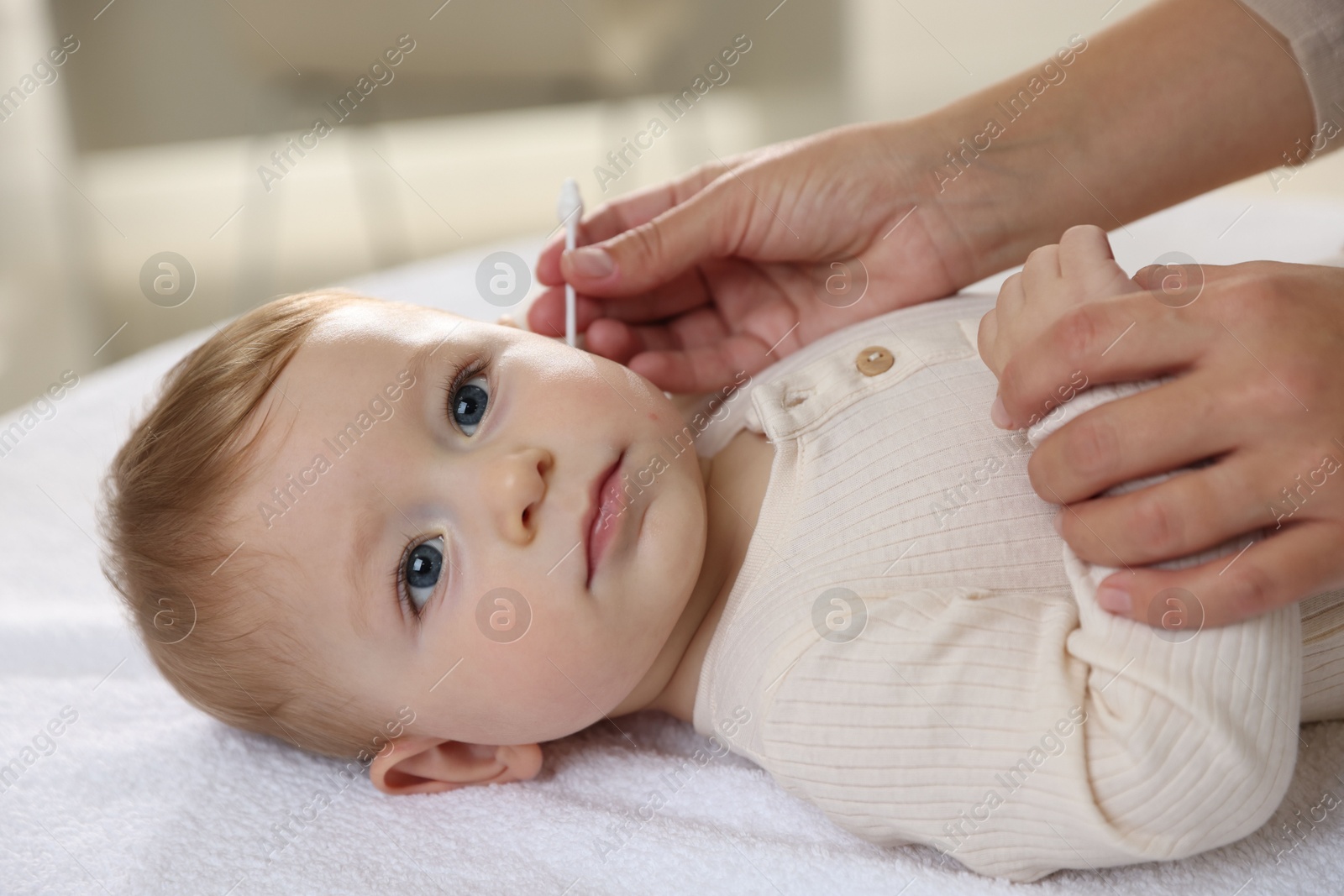 Photo of Mother cleaning ear of her cute little baby with cotton swab on bed, closeup