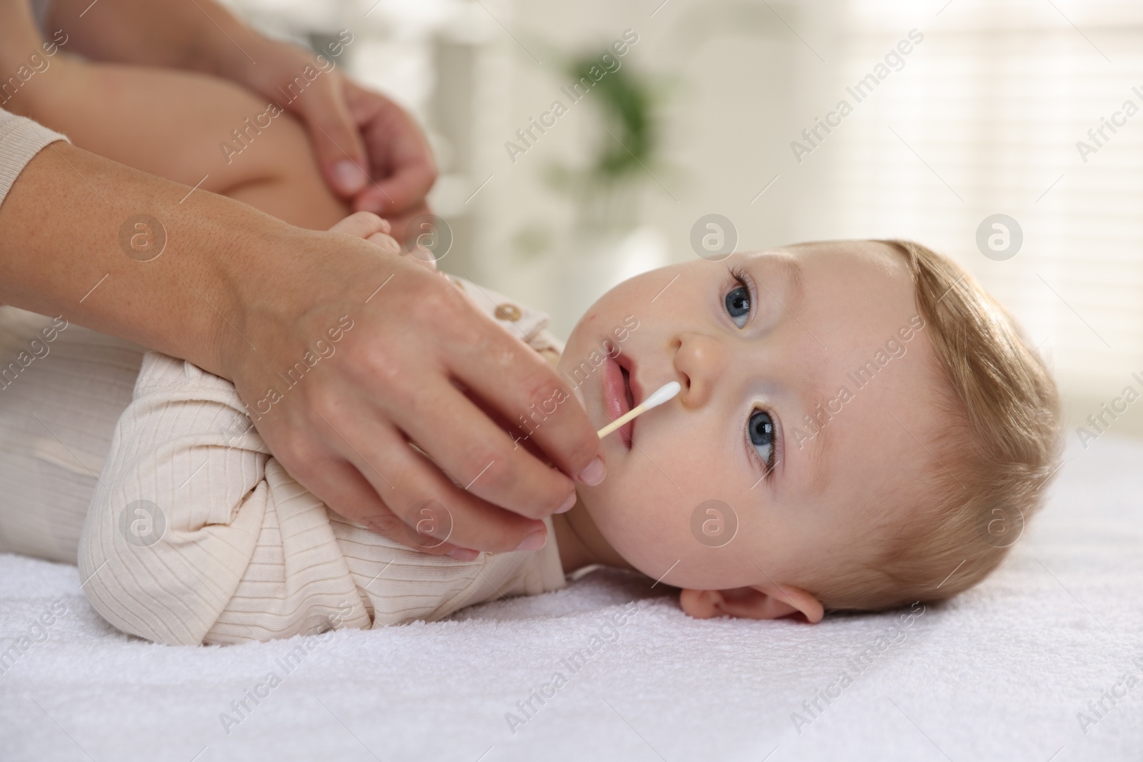 Photo of Mother cleaning nose of her cute little baby with cotton swab on bed, closeup