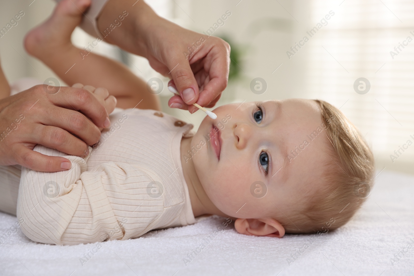 Photo of Mother cleaning nose of her cute little baby with cotton swab on bed, closeup