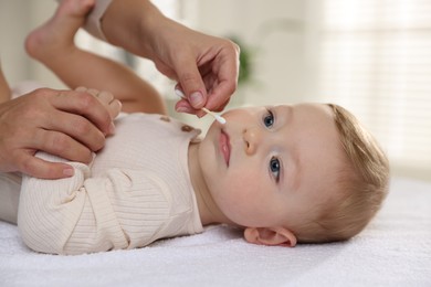 Photo of Mother cleaning nose of her cute little baby with cotton swab on bed, closeup