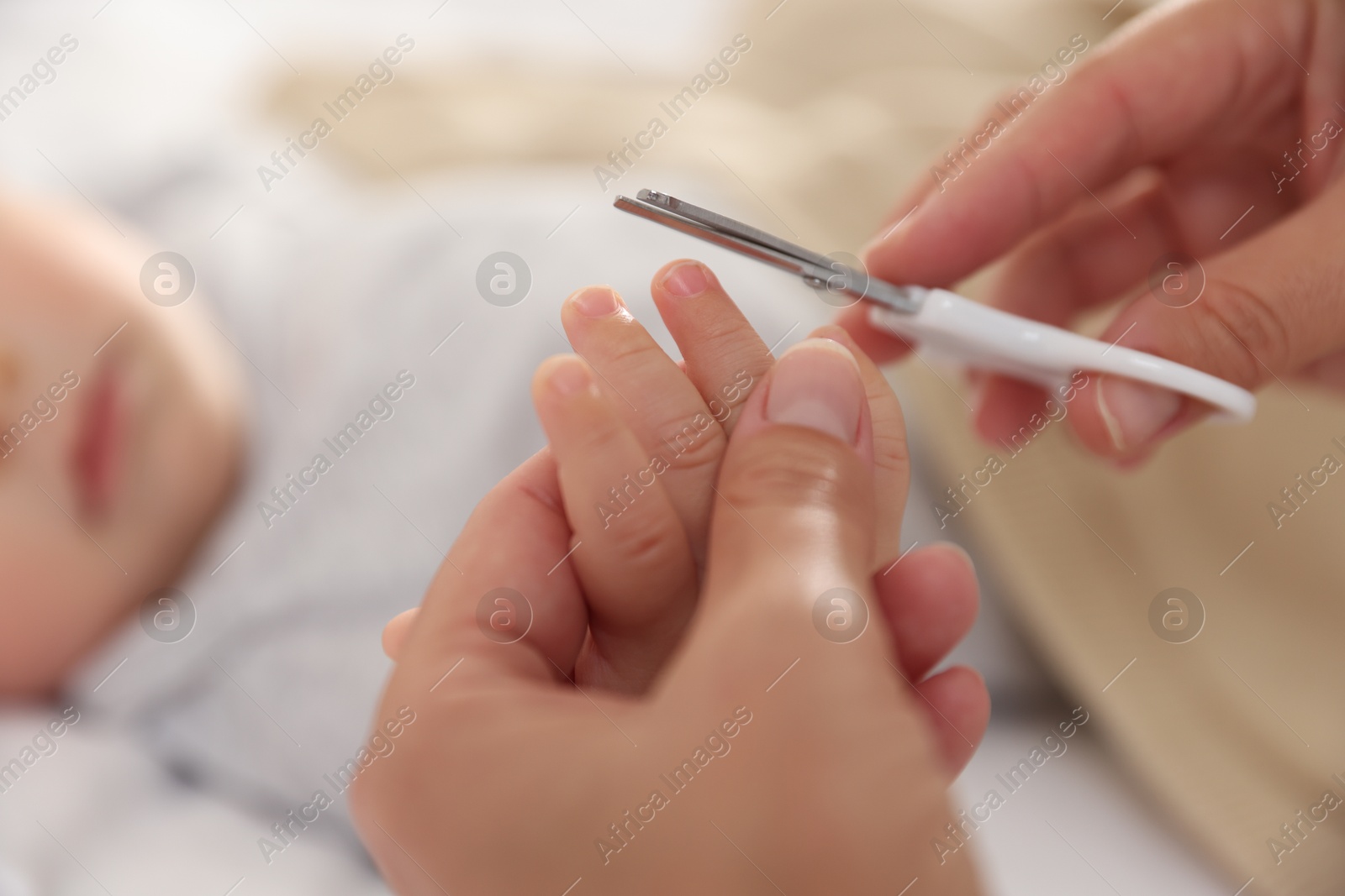 Photo of Mother cutting her cute little baby's nails on bed, closeup