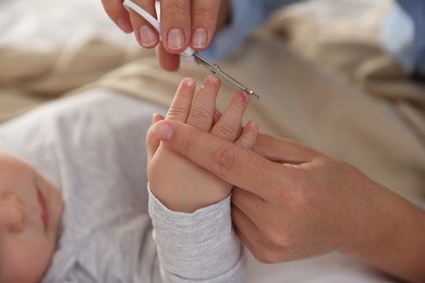 Photo of Mother cutting her cute little baby's nails on bed, closeup