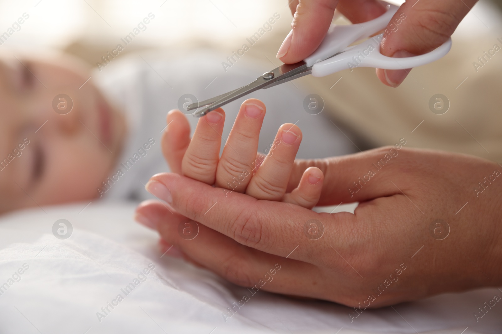 Photo of Mother cutting her cute little baby's nails on bed, closeup