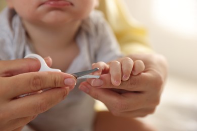 Mother cutting her cute little baby's nails at home, closeup