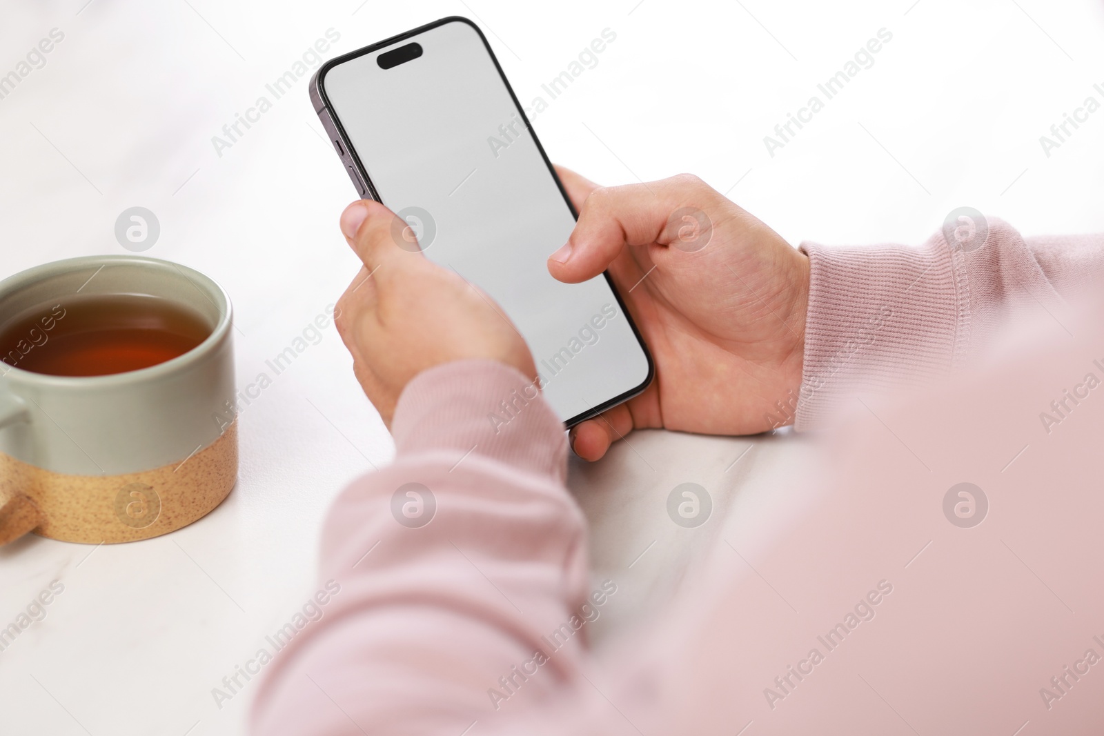 Photo of Man using smartphone at white table with cup of tea, closeup