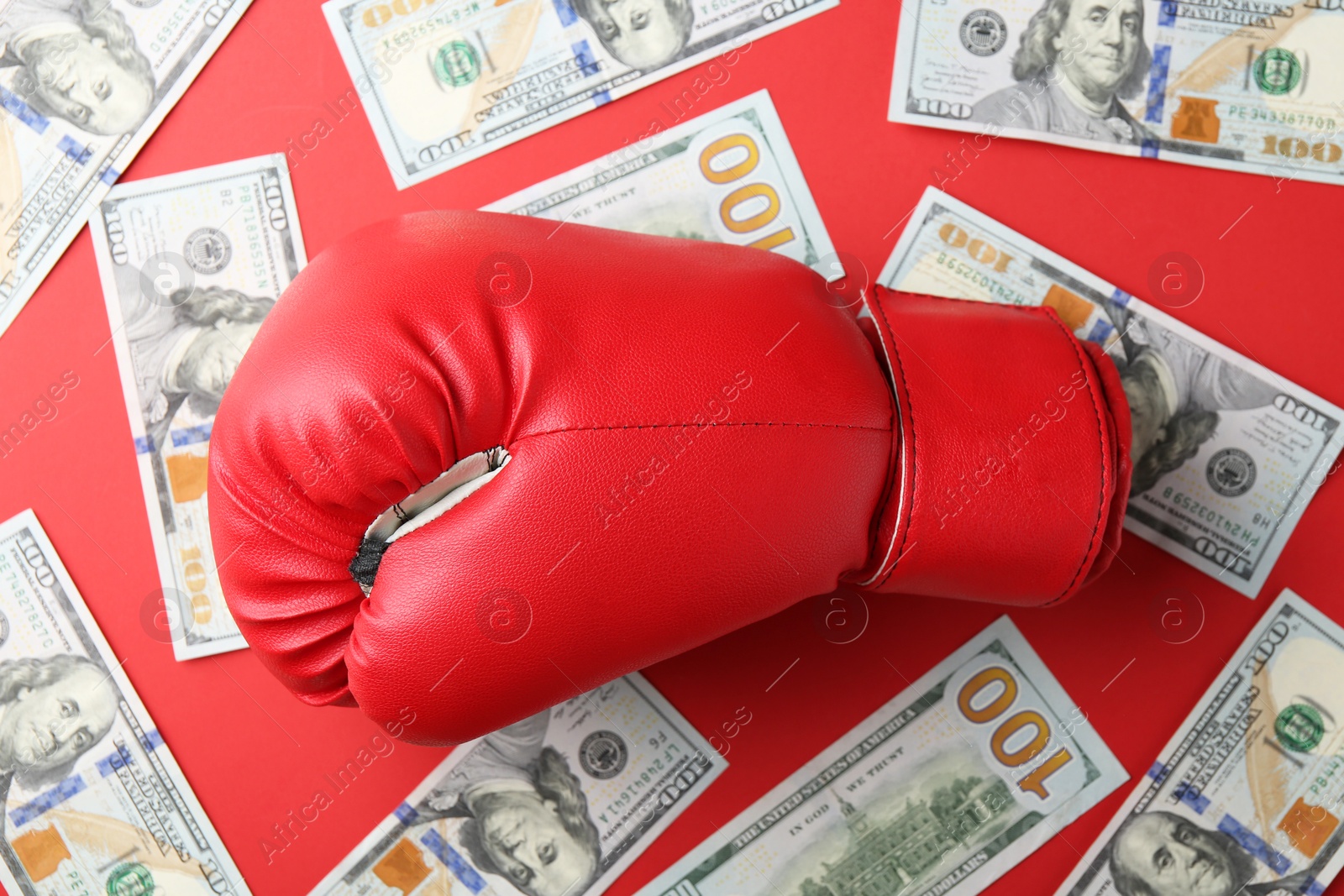 Photo of Boxing glove and dollar banknotes on red background, top view