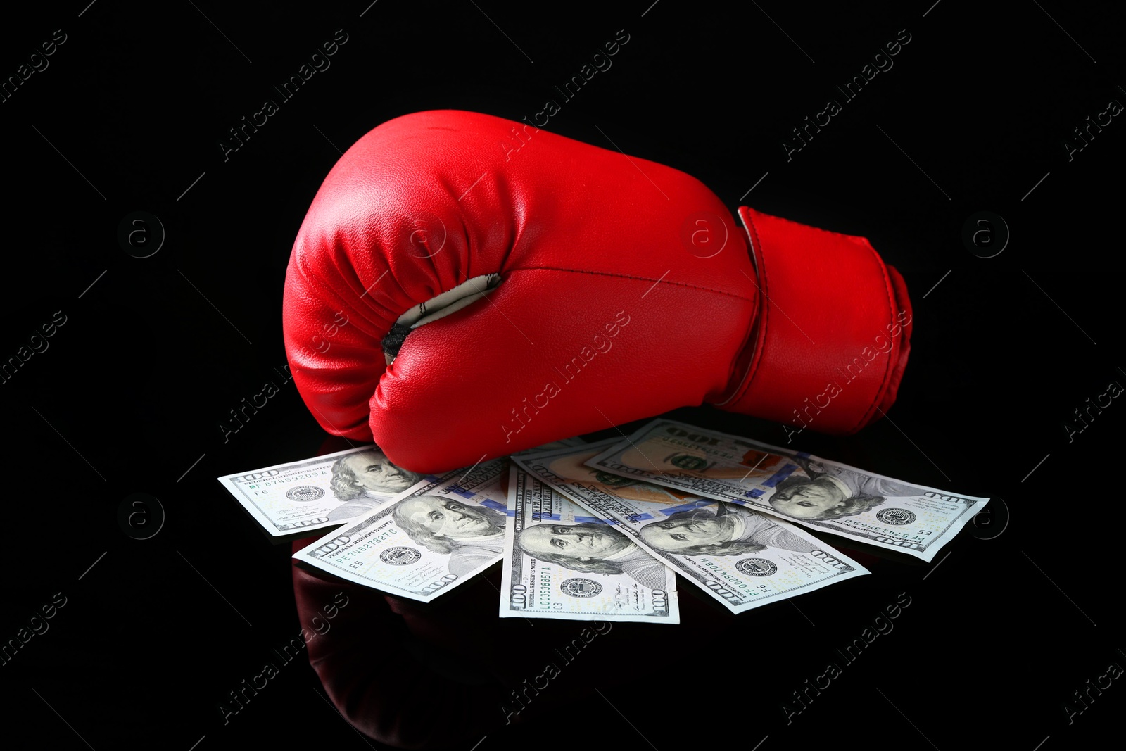 Photo of Red boxing glove and dollar banknotes on black mirror surface