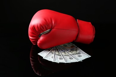 Photo of Red boxing glove and dollar banknotes on black mirror surface