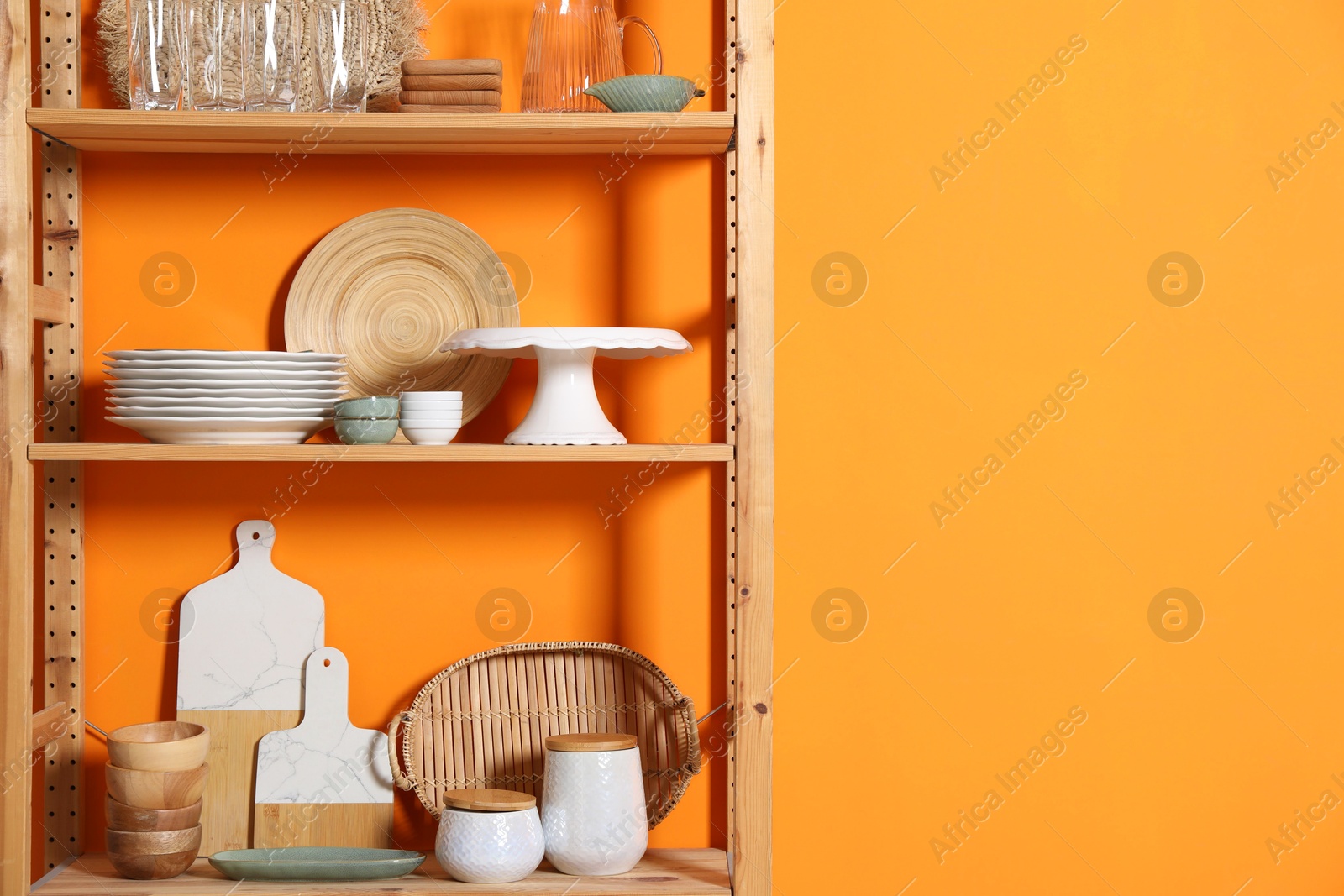 Photo of Wooden storage stand with kitchenware near orange wall indoors, space for text