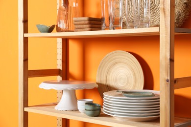 Photo of Wooden storage stand with kitchenware near orange wall indoors, closeup