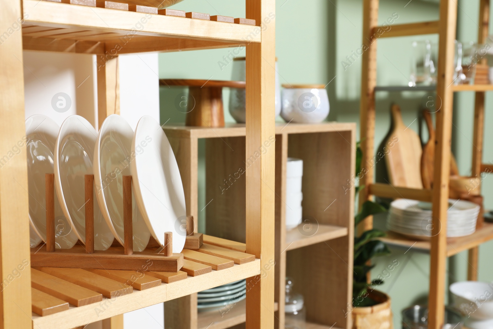 Photo of Wooden storage stands and shelving unit with kitchenware near green wall indoors, closeup