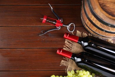 Photo of Wing corkscrew, bottles of wine, grapes and barrel on wooden table, top view. Space for text