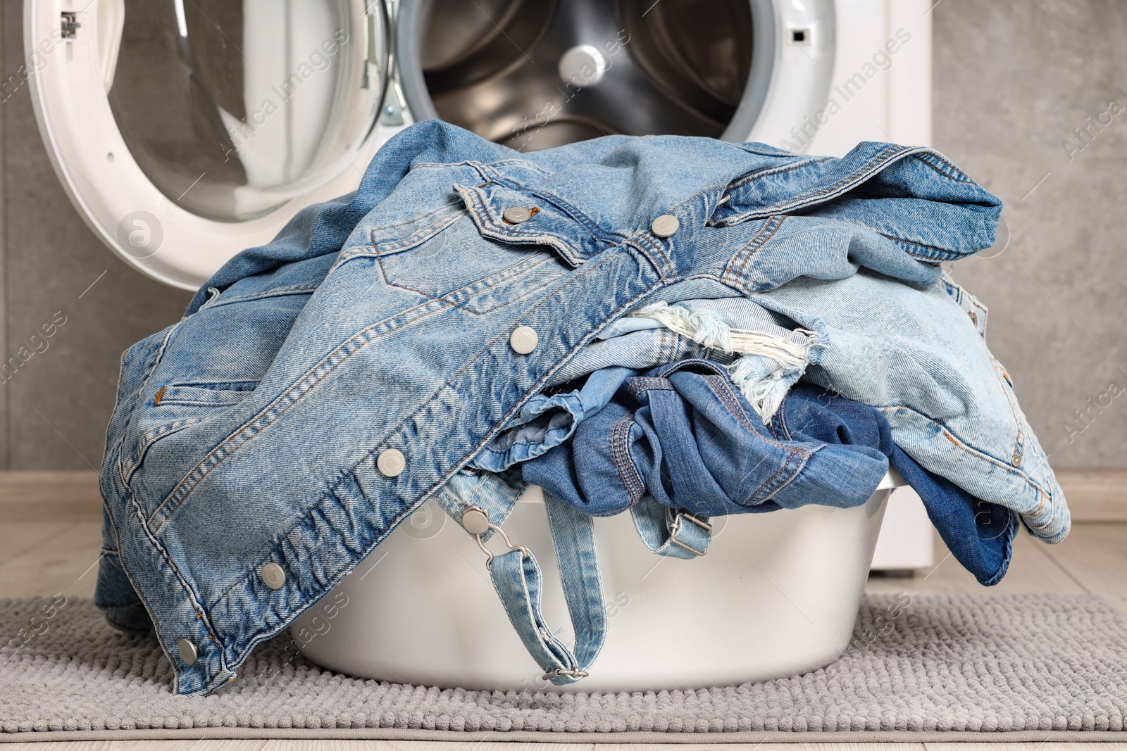 Photo of Washing machine and laundry basket with dirty denim clothes indoors