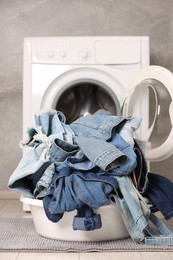 Photo of Washing machine and laundry basket with dirty denim clothes indoors