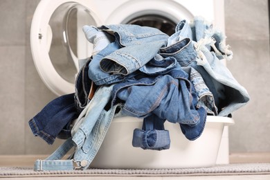 Photo of Washing machine and laundry basket with dirty denim clothes indoors