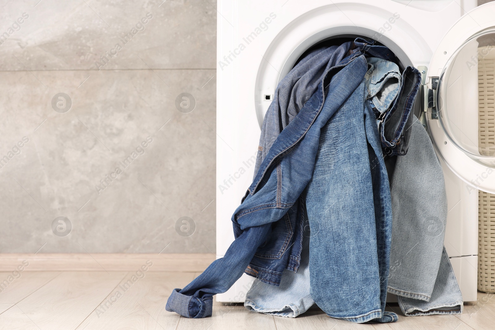 Photo of Washing machine with dirty jeans and other denim clothes indoors