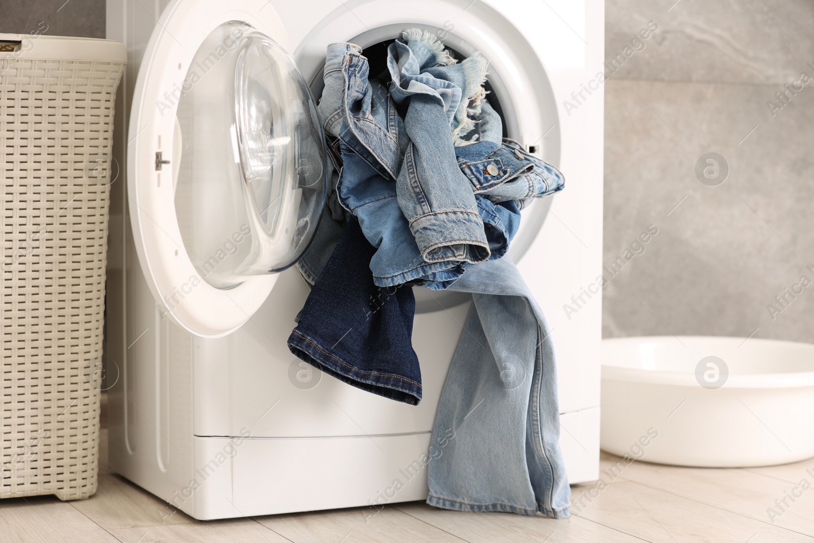 Photo of Washing machine with dirty jeans and other denim clothes indoors