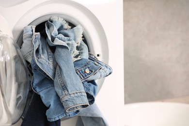 Photo of Washing machine with dirty jeans and other denim clothes indoors