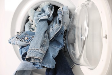 Washing machine with dirty jeans and other denim clothes, closeup