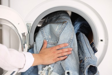 Photo of Woman putting dirty jeans and other denim clothes into washing machine, closeup