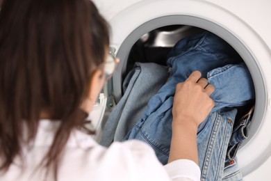 Woman putting dirty jeans and other denim clothes into washing machine, closeup