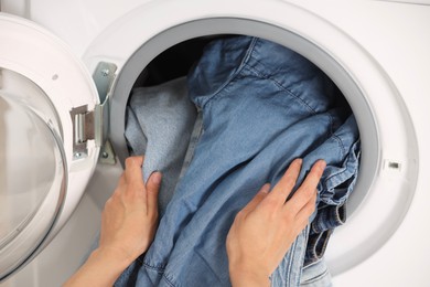 Photo of Woman putting dirty jeans and other denim clothes into washing machine, closeup