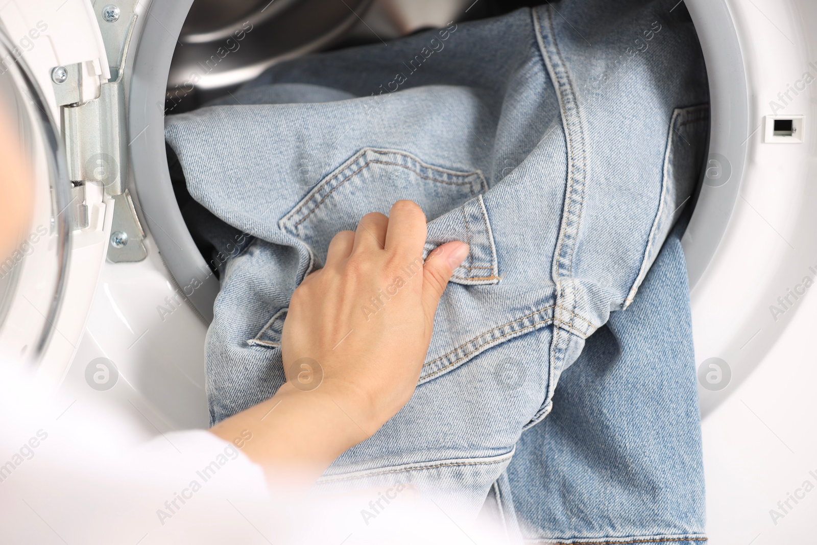 Photo of Woman putting dirty jeans and other denim clothes into washing machine, closeup