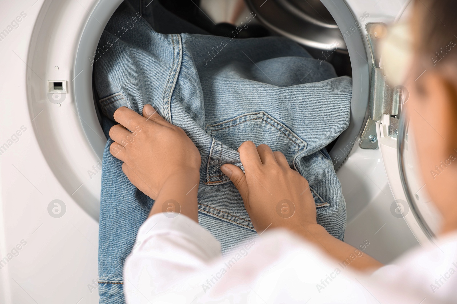 Photo of Woman putting dirty jeans and other denim clothes into washing machine, closeup