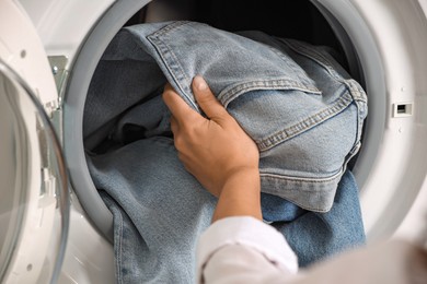 Photo of Woman putting dirty jeans and other denim clothes into washing machine, closeup