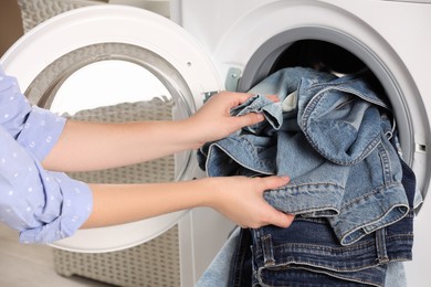 Woman putting dirty jeans and other denim clothes into washing machine, closeup