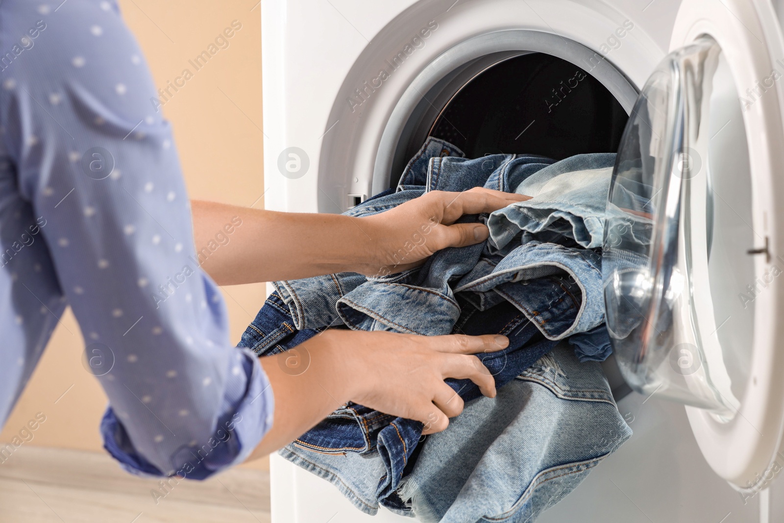 Photo of Woman putting dirty jeans and other denim clothes into washing machine, closeup