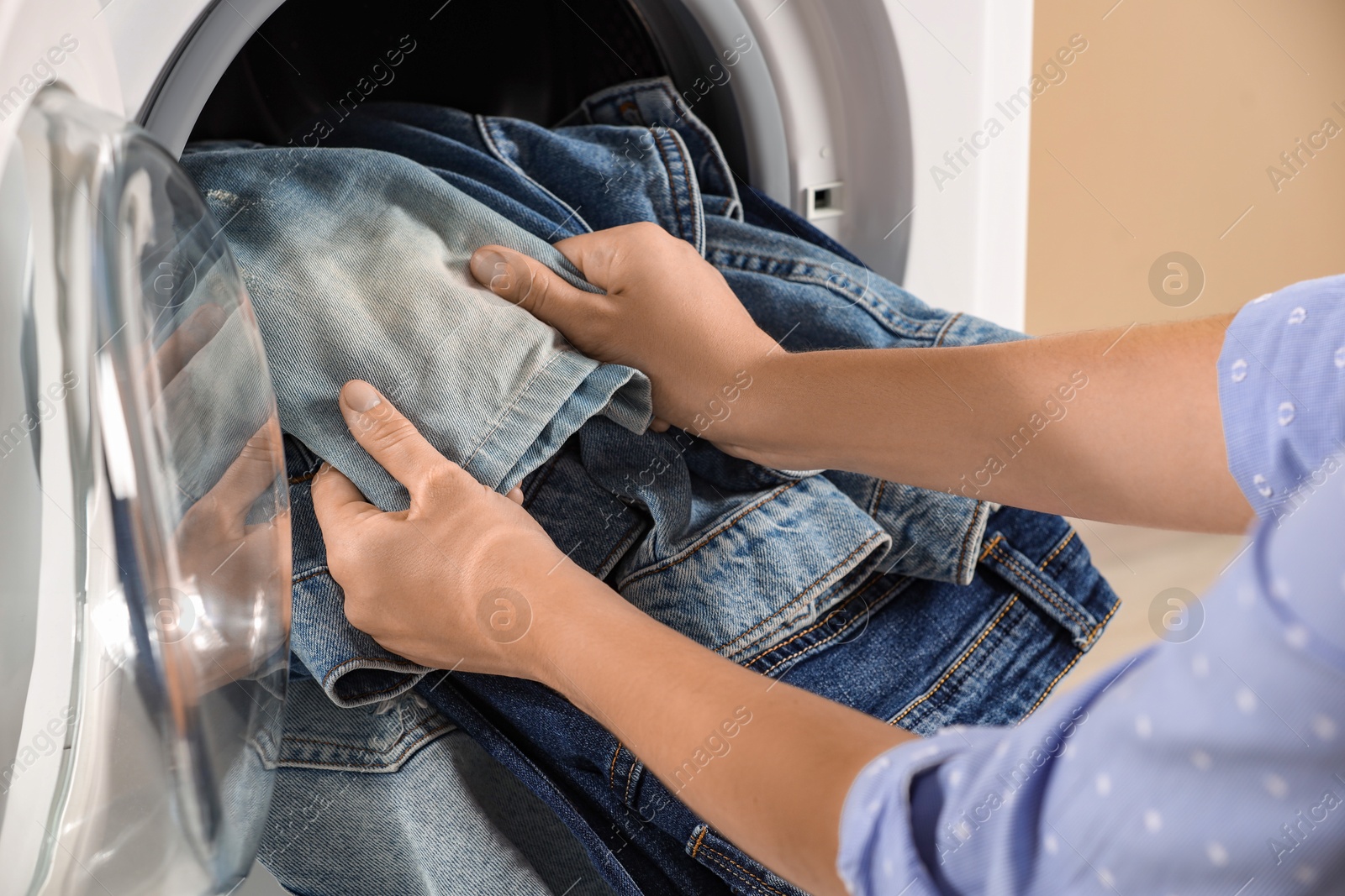 Photo of Woman putting dirty jeans and other denim clothes into washing machine, closeup